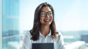 Mulher sorridente com óculos e cabelo castanho em escritório moderno.