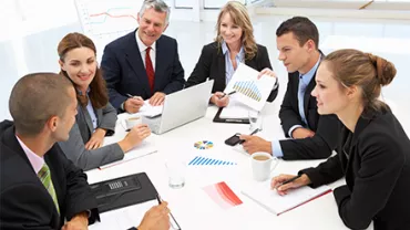 Grupo de pessoas em uma reunião com gráficos e laptops.