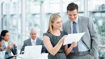 Dois colegas de trabalho analisando um documento na sala de reunião.