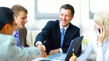 Grupo de pessoas em reunião de negócios, com homem sorrindo e apertando mãos.