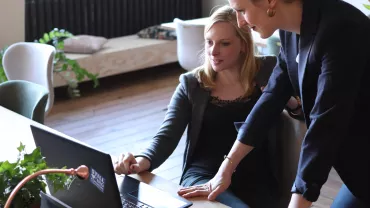 Duas mulheres discutindo um trabalho em frente a um laptop.