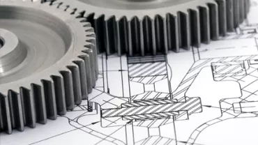 Engrenagens metálicas sobre um desenho técnico detalhado.