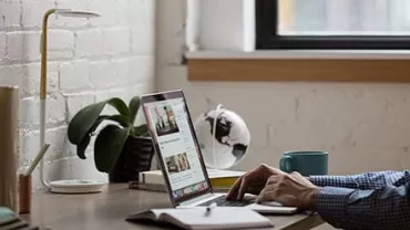 Pessoa usando laptop em uma mesa próxima à janela.