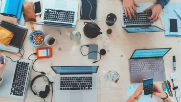 Mesa de trabalho com laptops, cadernos e xícara de café.