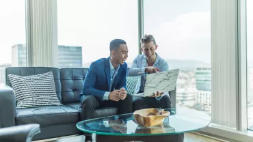 Dois homens sorrindo enquanto olham um laptop em um escritório moderno.