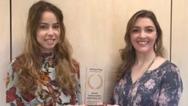 Duas mulheres segurando um prêmio. Ambas estão sorrindo.