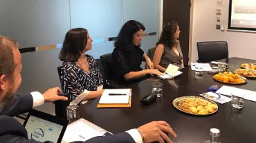 Reunião em sala de conferência com quatro pessoas e lanches na mesa.