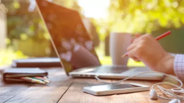 Pessoa trabalhando ao ar livre com laptop e smartphone.